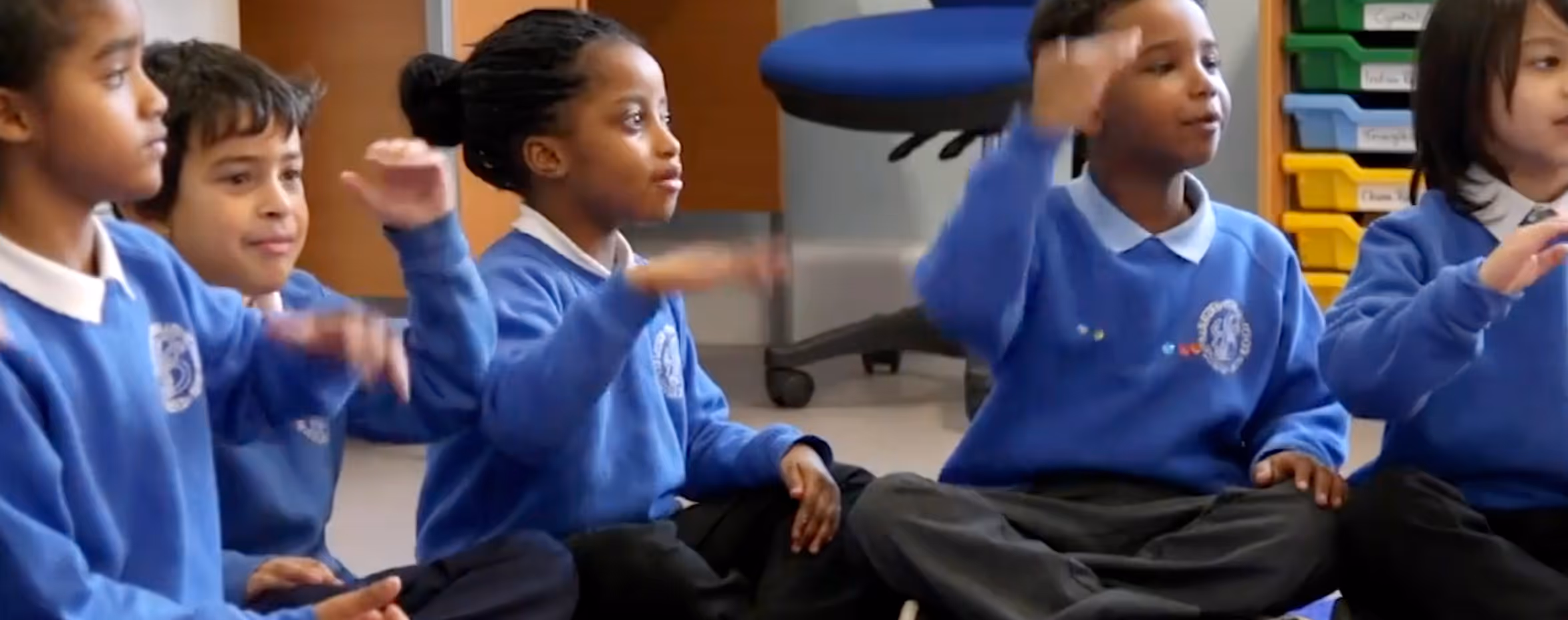 Children in blue school uniform, sitting on the floor, being active in a lesson